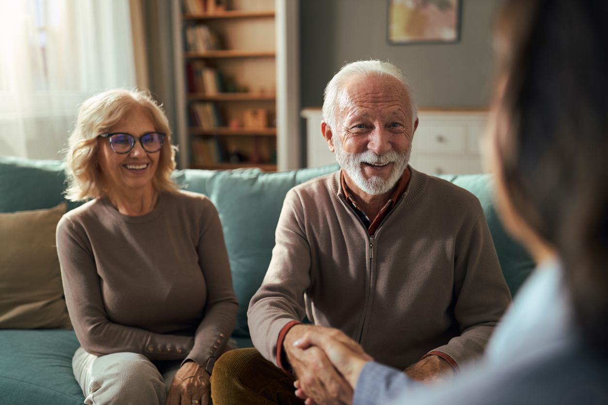 A retired couple shaking hands with their financial advisor during a meeting at home